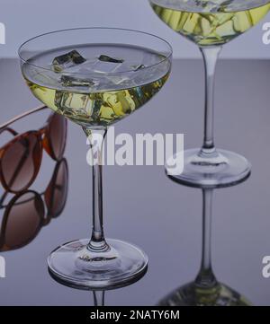 Coppia di cocktail con ghiaccio su una superficie riflettente con un paio di occhiali da sole. Foto Stock