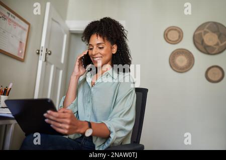Donna d'affari sorridente che usa un tablet e che parla al telefono a casa Foto Stock