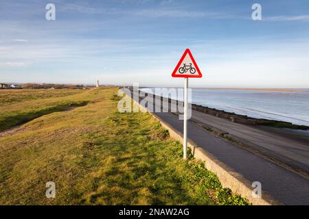 Wallasey, Regno Unito: Pista ciclabile che precede segnale triangolare di avvertimento sull'argine costiero, North Wirral Coastal Park. Foto Stock