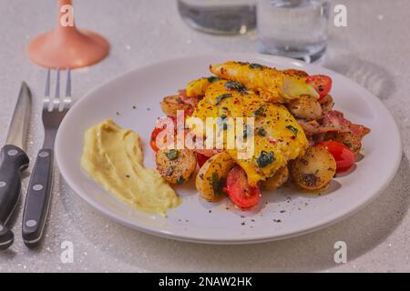 Filetto di eglefino con patate e verdure guarnite con erbe aromatiche e salsa di pesce. Foto Stock