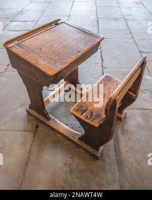 Sopravvissuto, vecchio stile vittoriano, scrivania scuola in legno con sedile rigido fisso e cerniera superiore seduto su un pavimento in pietra al Salts Mill, villaggio di Saltaire Foto Stock