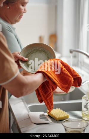 Uomo anziano che aiuta sua moglie, sta pulendo piatti puliti con un asciugamano morbido Foto Stock