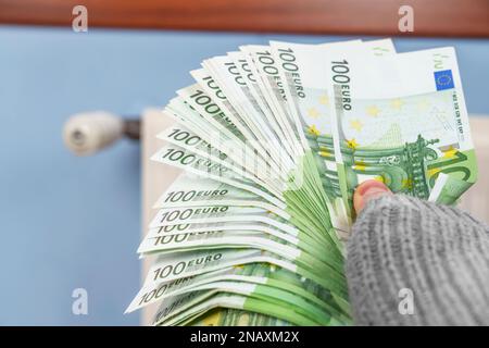 Soldi in mano in un maglione con un riscaldatore domestico. Il concetto di pagamento per il riscaldamento costoso e la crisi energetica in Europa Foto Stock