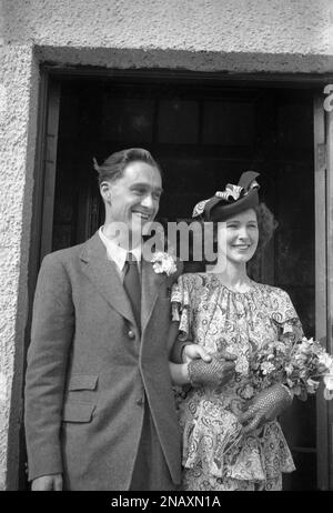 1950s, storico, una coppia recentemente sposata, in piedi insieme in una porta, sorridente, felice e tenendo le mani, la donna che indossa guanti di pizzo, abito floreale e grazioso cappello, Inghilterra, Regno Unito. Foto Stock