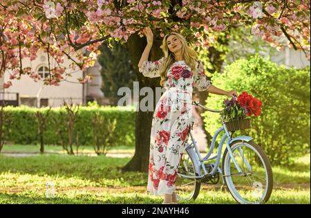 Romantico giro in bicicletta. Ragazza lungo vestito retro Cruiser bicicletta sakura albero. Vacanze primaverili. Concetto di turismo. Trasporto e viaggi. Stagione Sakura Foto Stock