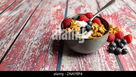 yogurt con muesli croccanti e lamponi e mirtilli in abola su fondo ligneo Foto Stock