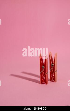 Primo piano di due clothespins rossi isolati e in piedi su sfondo rosa con spazio copia, in parte occupato dall'ombra di getto dei pioli Foto Stock