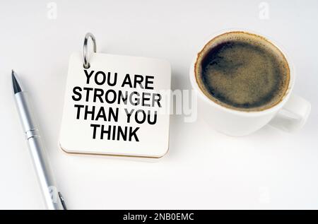 Concetto aziendale. Su una superficie bianca, una tazza di caffè, una penna e un blocco note con l'iscrizione: Sei più forte di quanto pensi Foto Stock