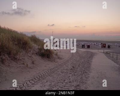 Una vista del paesaggio di sabbia vicino a una scogliera e sedie a sdraio sullo sfondo al tramonto sull'isola di Spiekeroog Foto Stock