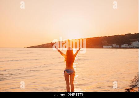 Silhouette felice bella giovane donna un lungo capello in un costume da bagno in piedi braccia stese sulla spiaggia al Tramonto Mare Adriatico, in Montenegro Foto Stock