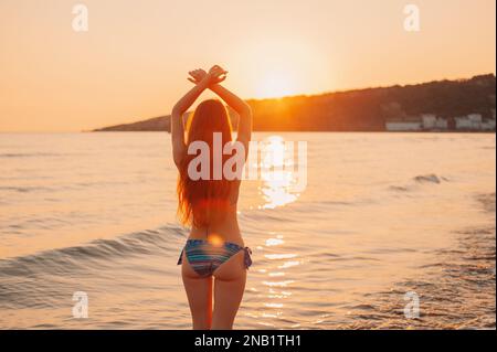 Silhouette felice bella giovane donna un lungo capello in un costume da bagno in piedi braccia stese sulla spiaggia al Tramonto Mare Adriatico, in Montenegro Foto Stock