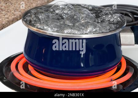 Pentola con acqua bollente sul bruciatore con mano sul fornello che mostra  la stufa non è caldo Foto stock - Alamy