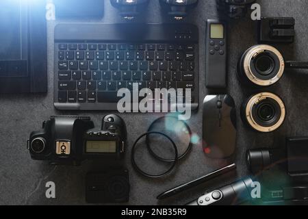 Workstation fotografica digitale su sfondo nero. Vista dall'alto di fotocamera digitale, flash, obiettivo e computer portatile. Attrezzature fotografiche professionali. Foto Stock