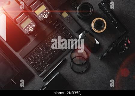 Workstation fotografica digitale su sfondo nero. Vista dall'alto di fotocamera digitale, flash, obiettivo e computer portatile. Attrezzature fotografiche professionali. Foto Stock