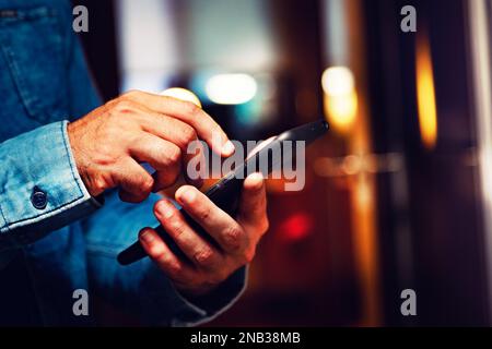 Invio di sms e condivisione di contenuti sui social network dall'interno della casa.immagine ravvicinata della mano dell'uomo che tiene il suo smartphone. Foto Stock