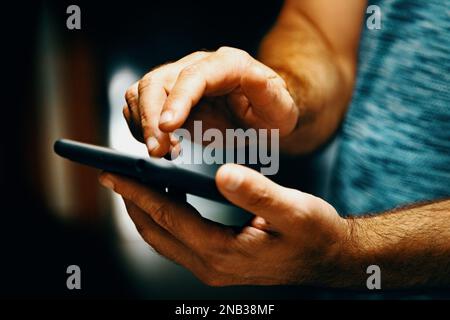 Invio di sms e condivisione di contenuti sui social network dall'interno della casa.immagine ravvicinata della mano dell'uomo che tiene il suo smartphone. Foto Stock