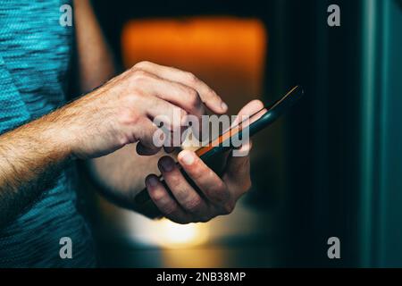 Invio di sms e condivisione di contenuti sui social network dall'interno della casa.immagine ravvicinata della mano dell'uomo che tiene il suo smartphone. Foto Stock