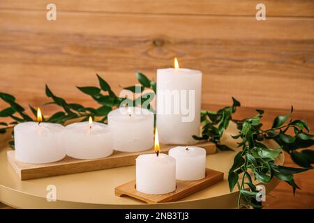 Candele brucianti con rami di pianta su tavolo vicino a muro di legno, primo piano Foto Stock