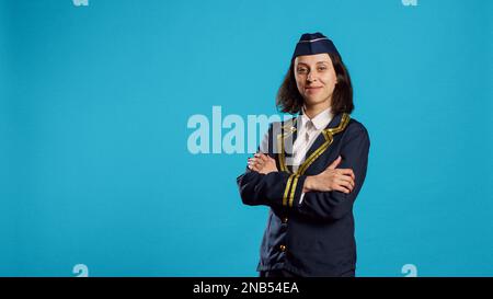 Donna felice Airliner che lavora come stewardess, indossando l'uniforme di aeronautica e posando con fiducia. Sorridente hostess aereo che si prepara per la rotta di volo commerciale, lavorando nel settore del volo. Foto Stock