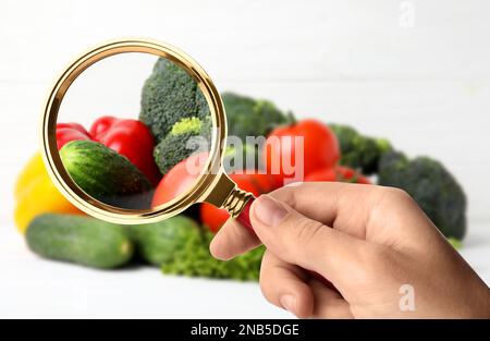 Donna con lente d'ingrandimento che esplora le verdure, primo piano. Rilevamento di veleni Foto Stock