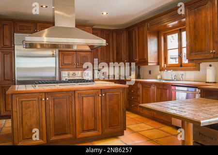 Armadietti in legno d'acero e isola con ripiani in marmo in cucina con pavimento in piastrelle di ceramica terracotta all'interno di una vecchia casa in stile regime francese del 1877. Foto Stock