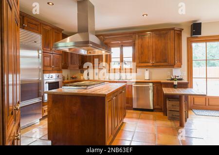 Armadietti in legno d'acero e isola con ripiani in marmo in cucina con pavimento in piastrelle di ceramica terracotta all'interno di una vecchia casa in stile regime francese del 1877. Foto Stock