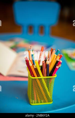 Un contenitore giallo con molte matite colorate è posto su un tavolo blu per bambini, accanto ad alcuni libri da colorare, ad una festa di battesimo Foto Stock