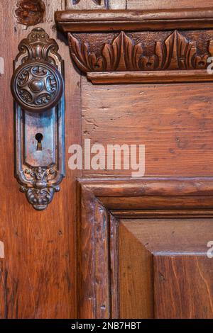 Primo piano dell'antico pomello in metallo sulla vecchia porta in legno con dettagli intagliati nel soggiorno all'interno della vecchia casa in pietra di campo in stile cottage del 1826. Foto Stock