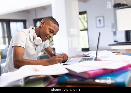 Immagine di felice ragazzo afro-americano che fa i compiti a casa con il portatile. Concetto di e-learning, istruzione e istruzione a domicilio. Foto Stock