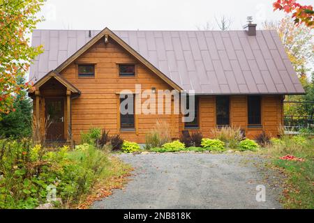 Pezzo sur pezzo Scozzs pino log casa facciata con marrone in piedi cucitura in lamiera tetto in autunno. Foto Stock