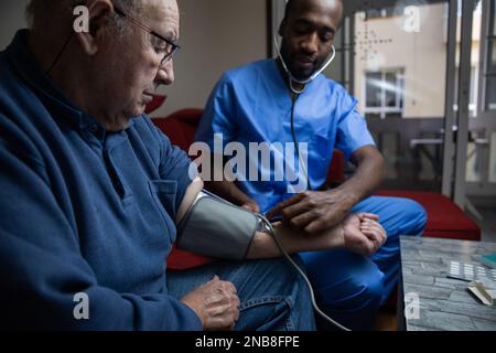 Un uomo anziano durante un medico di casa controlla la sua pressione sanguigna Foto Stock