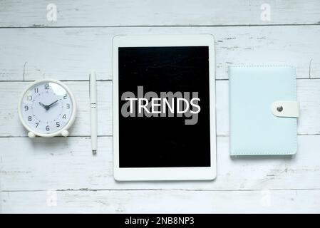 Nuovo concetto di business tecnologico. Vista dall'alto dell'orologio, della penna, del notebook e del tablet con Trends su sfondo di legno bianco. Foto Stock