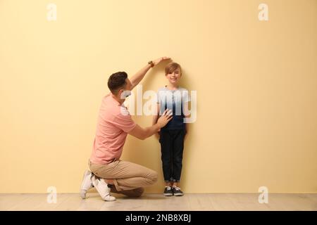 Padre che misura l'altezza del figlio vicino a una parete beige all'interno Foto Stock