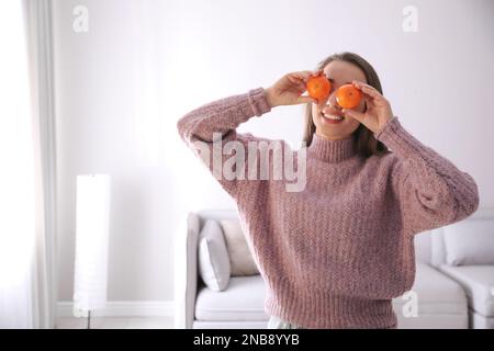 Giovane donna felice con i tangerini maturi freschi a casa Foto Stock