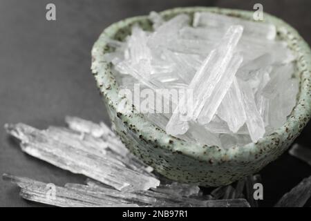 Cristalli di mentolo in ciotola su fondo grigio, primo piano Foto Stock