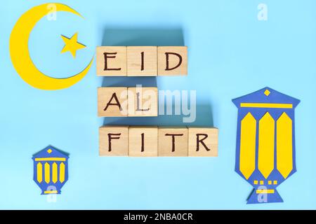 Luna di Crescent, stella e lanterna decorazione con testo su blocchi di legno piatto giacente su sfondo blu. EID al fitr celebrazione del mese santo islamico. Foto Stock