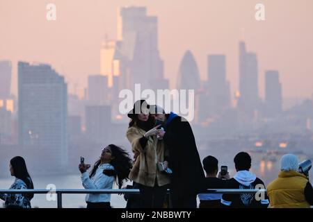 Londra, Regno Unito. 13th febbraio, 2023. Una coppia prende un selfie con gli edifici della City of London come sfondo. Al Greenwich Park sono state osservate condizioni di vago durante il tramonto e il tramonto, poiché i venti meridionali dovrebbero portare depositi di polvere sahariana nel Regno Unito, che raggiungeranno il picco massimo tra martedì e mercoledì. La polvere minerale nell'atmosfera può trasformare il cielo in una tonalità arancione, causando 'pioggia di sangue' e spettacolari albe e tramonti. Credit: Undicesima ora di Fotografia/Alamy Live News Foto Stock