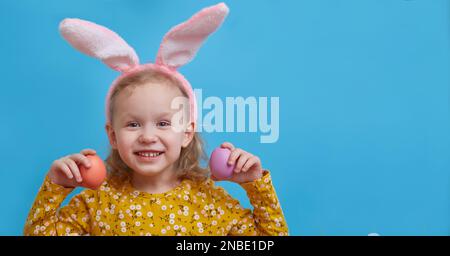 Carina ragazza felice con orecchie coniglietto e tenendo colorate uova di pasqua davanti ai suoi occhi. Carta di Pasqua e concetto Foto Stock