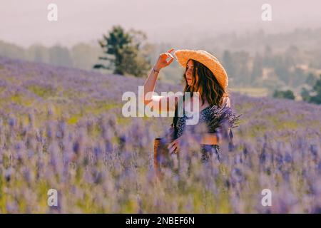Ritratto di donna in un cappello di paglia in piedi in campo di fiori di lavanda, guardando in lontananza Foto Stock