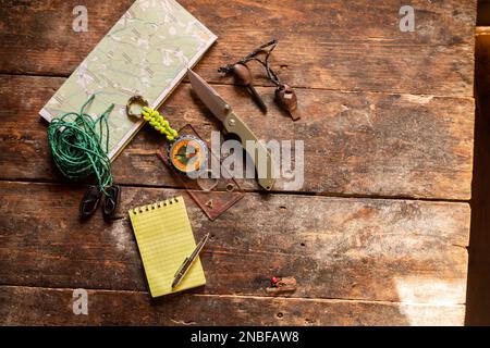 Blocco note e penna a sfera. Attrezzatura turistica su un vecchio tavolo di legno. Bussola, coltello e mappa per turisti. Foto Stock