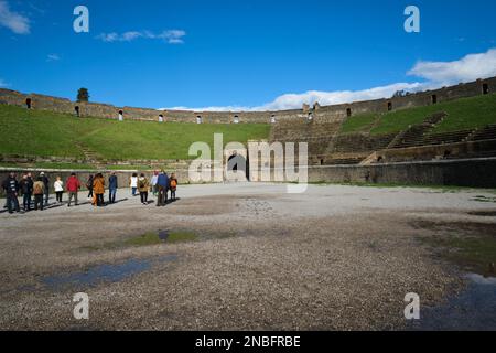 I turisti che visitano l'interno dell'anfiteatro coperto di erba. Al Parco Archeologico di Pompei vicino a Napoli, Italia. Foto Stock
