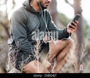 Scelta di una playlist che si adatti al calmo umore della natura. un giovane uomo sportivo che indossa gli auricolari mentre usa un cellulare all'aperto. Foto Stock