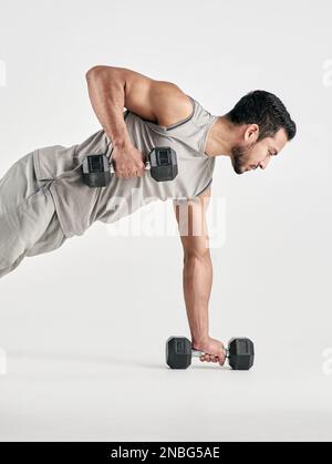 Supera i limiti percepiti. Studio shot di un giovane uomo muscolare che si esercita con manubri su uno sfondo bianco. Foto Stock