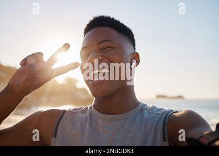 Selfie, fitness e pace con un uomo nero sulla spiaggia per un allenamento cardio o di resistenza durante l'estate. Ritratto, mano segno e esercizio con un maschio Foto Stock