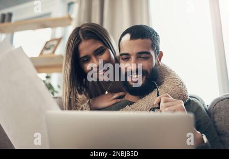 Organizzare le proprie spese in un unico posto. una giovane coppia che usa un notebook mentre passa attraverso la documentazione a casa. Foto Stock