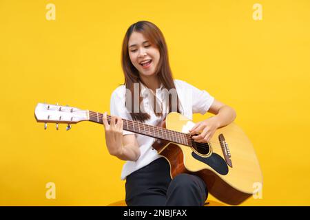 Le donne suonano la chitarra acustica e cantano la canzone su sfondo giallo isolato. Foto Stock