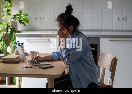Una giovane donna addormentata si siede alla scrivania sfrega gli occhi stanchi per lavorare online o studiare a lungo con un computer portatile Foto Stock