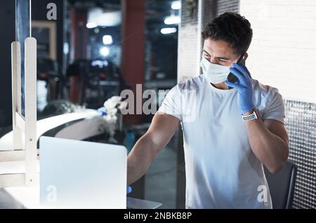 Far conoscere ai suoi clienti i nuovi protocolli di palestra. un giovane uomo che indossa una maschera facciale mentre lavora in palestra. Foto Stock