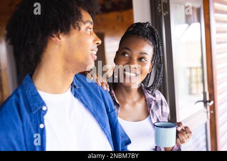 Coppia africana felice americana che spende il tempo nella cabina del ceppo che beve il caffè. Cabina di legno, natura e concetto di stile di vita. Foto Stock