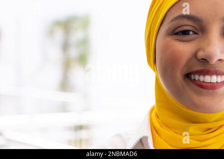 Ritratto di felice donna d'affari biraciale con hijab in ufficio moderno. Concetto globale di business, finanza e ufficio. Foto Stock